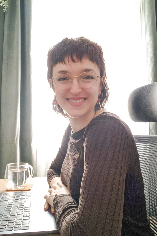 Beatriz sonríe frente a su ordenador en el que realiza optimizaciones SEO y diseño gráfico.